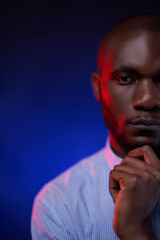 Cropped closeup portrait of a African American man in blue shirt. Studio portrait on a dark background illuminated by red and blue light
