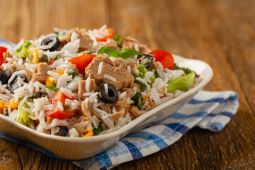 Italian tuna salad with rice, olives and capers. Front view. Natural wooden background.