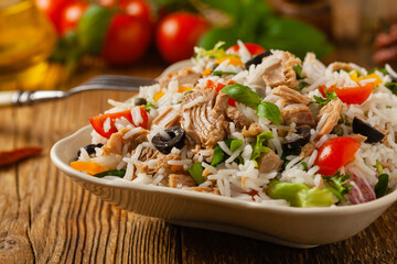 Italian tuna salad with rice, olives and capers. Front view. Natural wooden background.