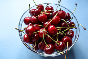 Naklejka na ściany i meble Ripe cherries in a Cup close-up on a blue background, top view-the concept of eating healthy fruits