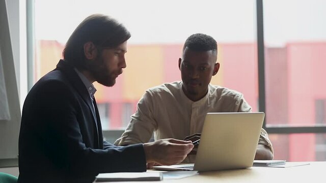Male caucasian manager teacher mentor wear suit consulting client teaching helping african american intern training explaining online project pointing on laptop at office meeting, apprentice concept