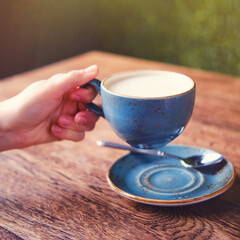 Woman hand holding a cup of latte coffee in a summer cafe, close up