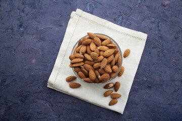 Almond in a bowl on white serviette. Violet grunge background, view from above.
