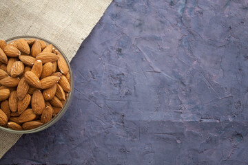 Almond in a bowl and piece of sackcloth in the left side of violet grunge background
