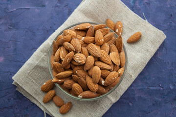 Almond in a bowl on piece of sackcloth. Violet grunge background, view from above.
