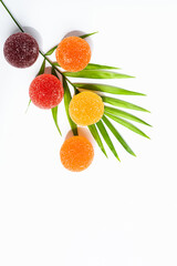Colored balls of fruit marmalade on a white background with a palm branch. copy space.