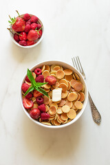 Mini pancake cereal with berry and mint leaves on white background.