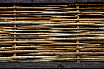 Decorative cladding of the building made of brown-colored wood. A wicker wall of rods with bark
