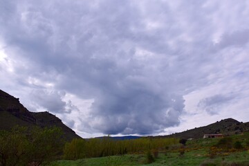Mountain landscape with almond trees, poplars, holm oaks, cow pen and in the background the Port of Oncala. Cloudy sky.