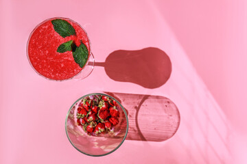 Strawberry smoothie or alcohol cocktail in wineglass decorated with mint and flowers on pink background.