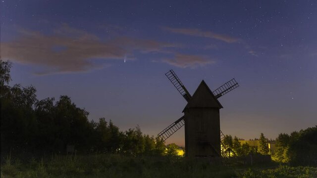 Comet C/2020 F3 (NEOWISE) pass over old , wooden windmill in rural scenery. Time lapse of moving night stars and comet. Crearly visible moving speed difference between stars and comet