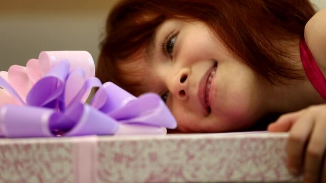 Cute happy little girl child kid looks holding a huge present gift box wrapped in purple violet ribbon bow in close up