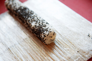 Sushi with black sesame seeds and cream cheese before being cut into pieces on the table close-up.