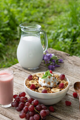 Summer Breakfast of cereals with grapes, milk and berry yogurt outdoors in nature. Vegetarian morning Breakfast on the background of green grass.