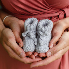 A man father holds the hands of a woman's mother in his arms against the background of a pregnant belly. Parents hold little booties in their hands