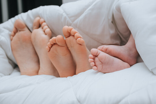 Close-up of the legs of the family of mom, daughter and little newborn son, covered with a plaid. Sleeping family. Time to sleep. Photography, concept.