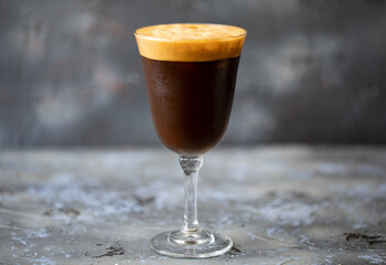Cold coffee in glass with foam on grey-blue background