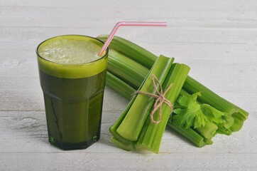 Fresh green celery juice in glass on white wooden background