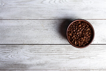 Arabica coffee beans in brown bowl on white wooden desk. Close-up, copy space, top view, background. Coffee roast, caffeine concept