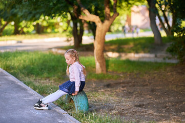 Naklejka na ściany i meble A girl sits in the park on a wheel in sneakers. Girl with blond hair walks in the park and thinks