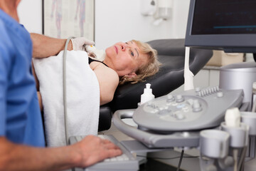 Mature woman patient undergoing examination thyroid lying by elderly man doctor with ultrasonography device