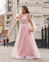 Fototapeta premium Young beautiful woman wearing long pink dress. Outdoor fashion full length portrait.