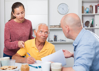 Obraz premium Image of mature man at table in home kitchen filling up documents with family