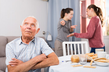 Upset elderly man sitting, young woman with mother havilng conflict on background