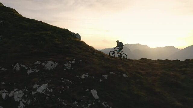 Aerial - Extreme sport male cyclist trying to paddle up the difficult mountain terrain at sunset. 4K