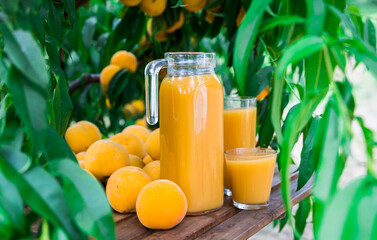 still life of ripe appetizing yellow peaches and jug of freshly squeezed peach juice on table in garden