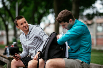 Fit young men taking rest from running. Two friends training outdoors.	