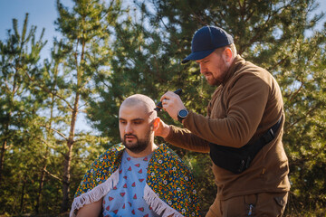 Fototapeta premium Tough red bearded guy shaving bold the other man outdoors in the pine forest