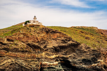 Old white lighthouse Akra Tamelos on majestic cliff on Kea Island, view from the sea with blue sky on sunny day, Greece. 