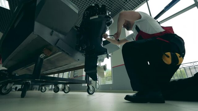 Male worker is mending boat's engine in the workshop
