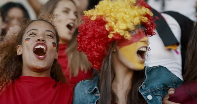 Happy German soccer supporters singing together in stadium. Group of fans with their arms around singing and swinging in fan zone during a live game.
