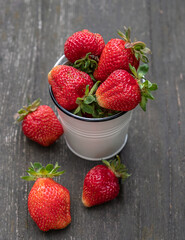 Still life with fresh juicy ripe strawberries in a white little bucket on a wooden background.