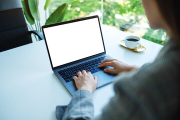 Mockup image of a businesswoman using and typing on laptop keyboard with blank white desktop screen in the office