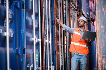 Young confident Caucasian man engineer using laptop computer and wearing white safety helmet and check for control loading containers box from Cargo freight ship for import and export, transport