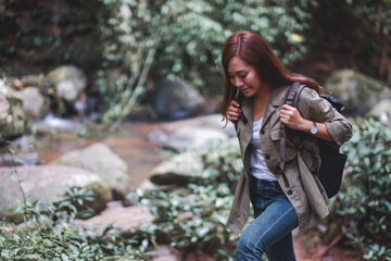 Fototapeta na wymiar A female traveler with backpack walking by mountain stream for hiking concept
