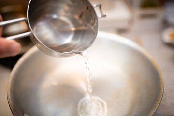 計量カップから鍋に水を注ぐ