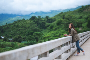 Fototapeta na wymiar A beautiful young asian woman standing on the bridge and looking at mountains and nature view