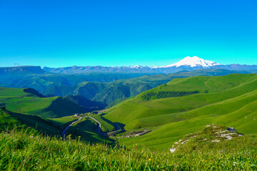 Fototapeta na wymiar Elbrus and Green Meadow Hills at a Summer Day. North Caucasus, Russia