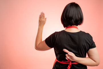 Woman employed at supermarket with red apron and black t-shirt showing fake oath cross finger from...
