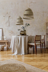 Stylish and elegant dining room interior with diner table, design chairs, rattan pendant lamps, dried flowers in vases, furniture, decoration and elegant personal accessories in cozy home decor.