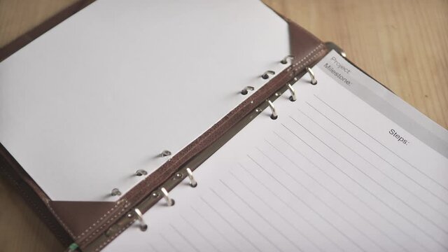 Close up shot of woman hands opening metal steel binder on leather cover note book pad daily planner organizer journal