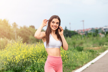 Naklejka na ściany i meble Portrait of a young woman in sportswear talking on phone outdoors while taking break between training,