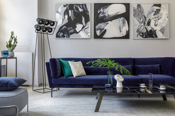 Stylish and modern living room interior with blue velvet sofa, mock up paintings, design furniture, plant, table, decoration, concrete floor, elegant personal accessories in home decor.