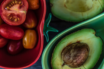 Two bowls that are adapted for tomatoes and avocados out on a table