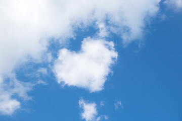 Fluffy white clouds float across the blue sky on a clear sunny summer or spring day. Background sky. Heart shaped cloud. Low angle view