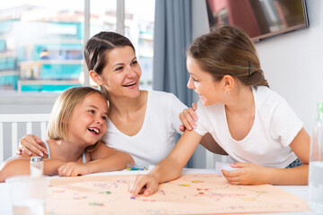 Two sisters play board game at home with their mother